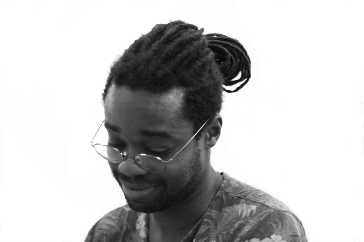 Person with dreadlocks and glasses smiling slightly.