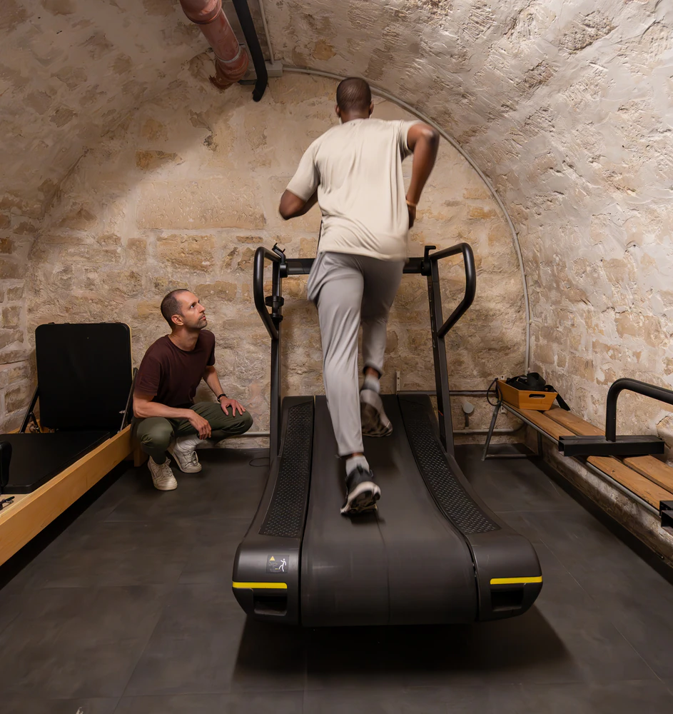 Man running on treadmill in stone-walled gym.
