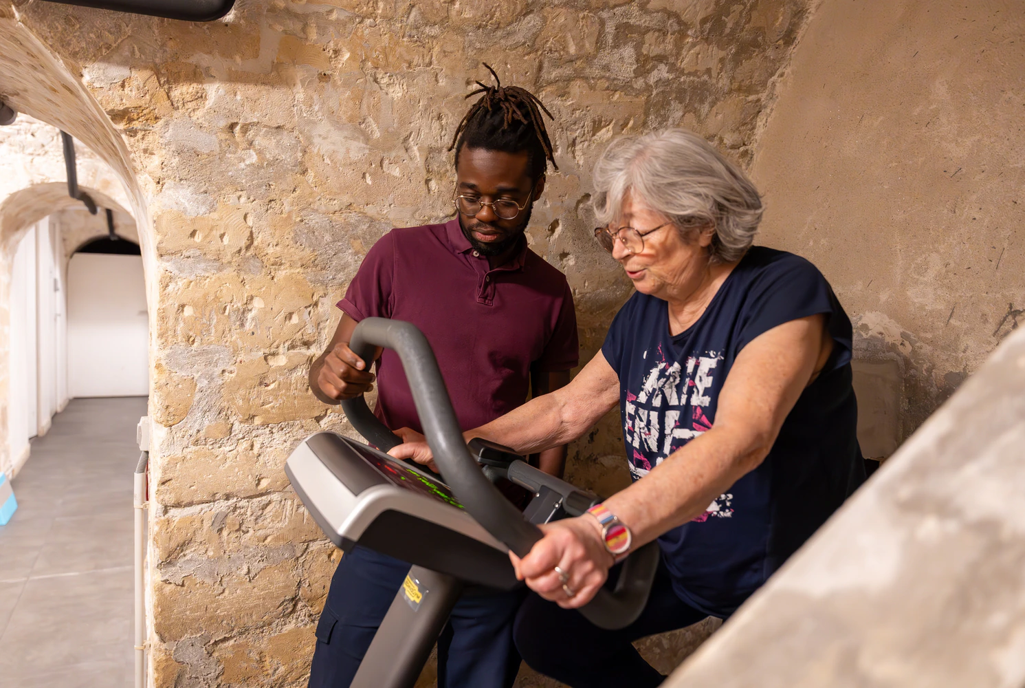 Older woman using exercise machine with trainer's help.
