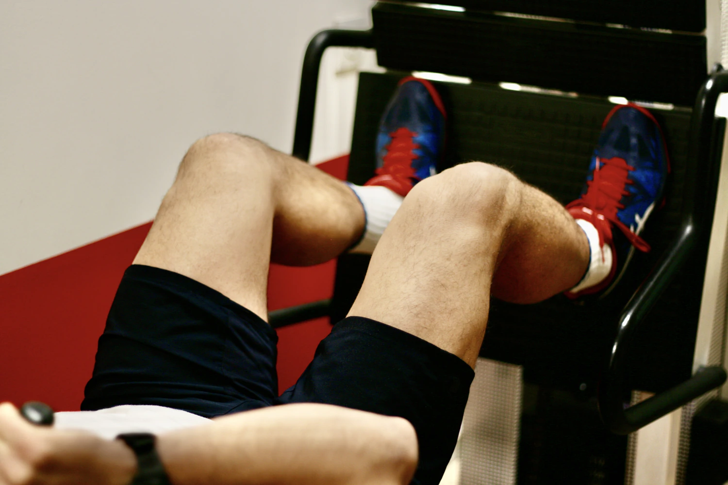 Leg press exercise with red shoes and black shorts.