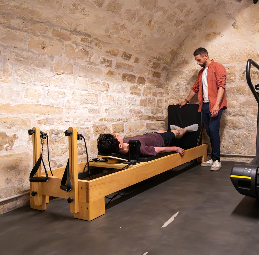 Person exercising on pilates reformer with trainer guidance.