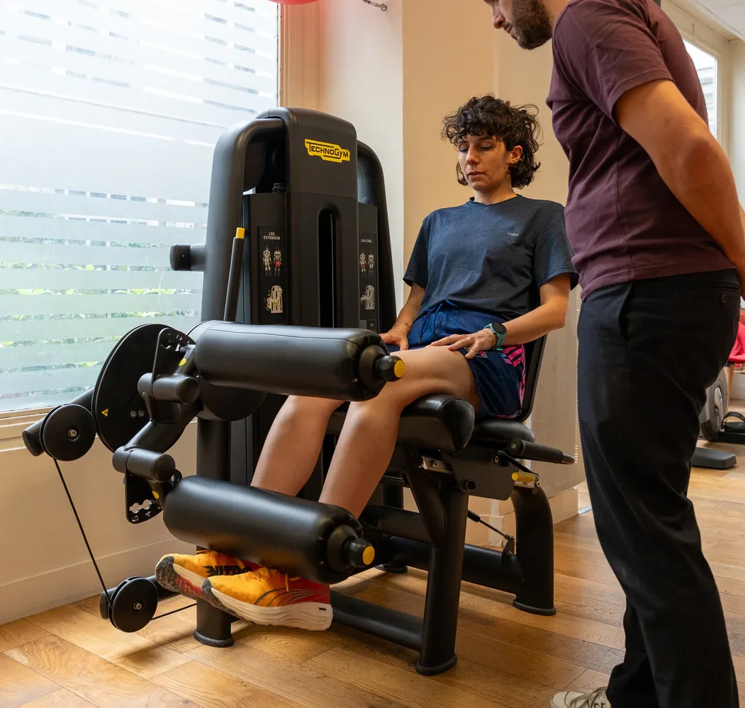 Person using leg extension machine with trainer guidance.